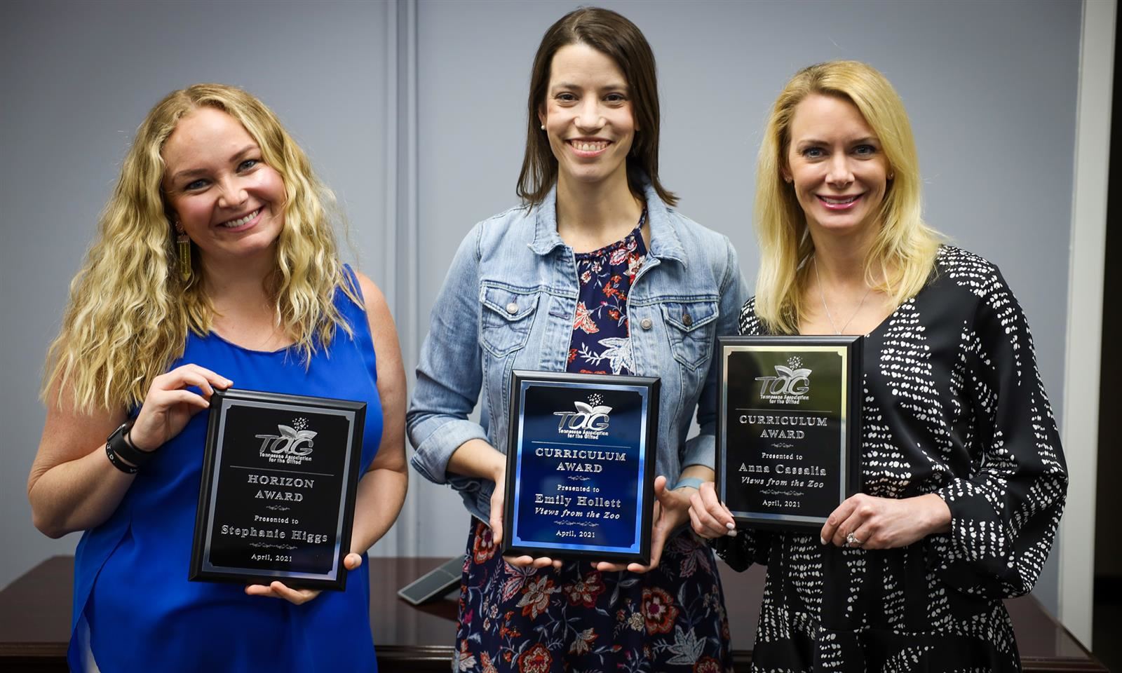 Three teachers stand for a photo and hold plaques
